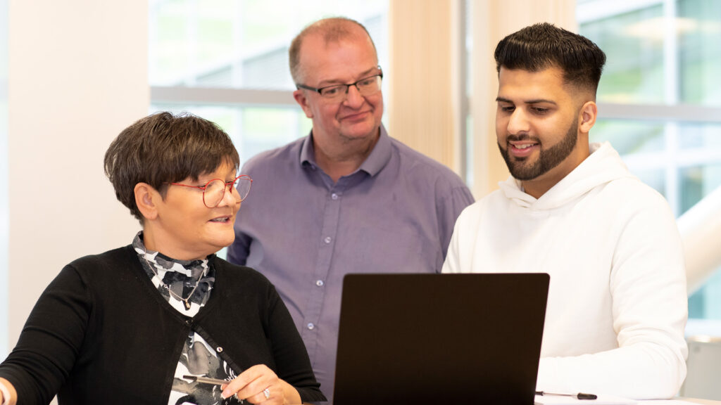 Three members of staff gathered around a laptop