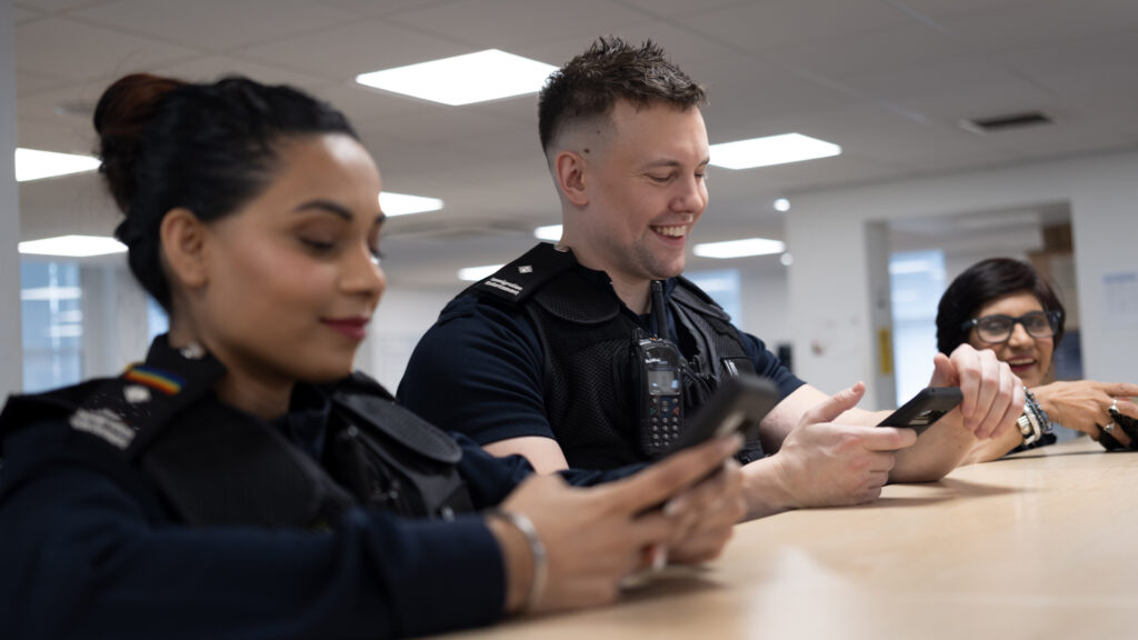 Three Immigration Enforcement Officers looking at mobile devices in an office setting