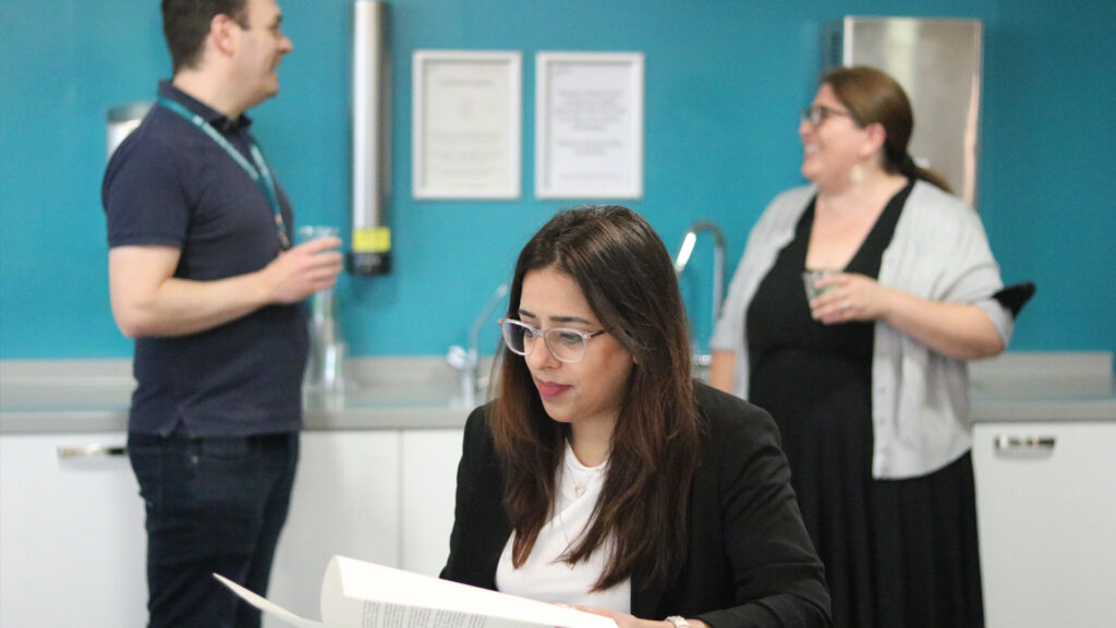 Member of Home Office staff reading a document while 2 more talk in the background
